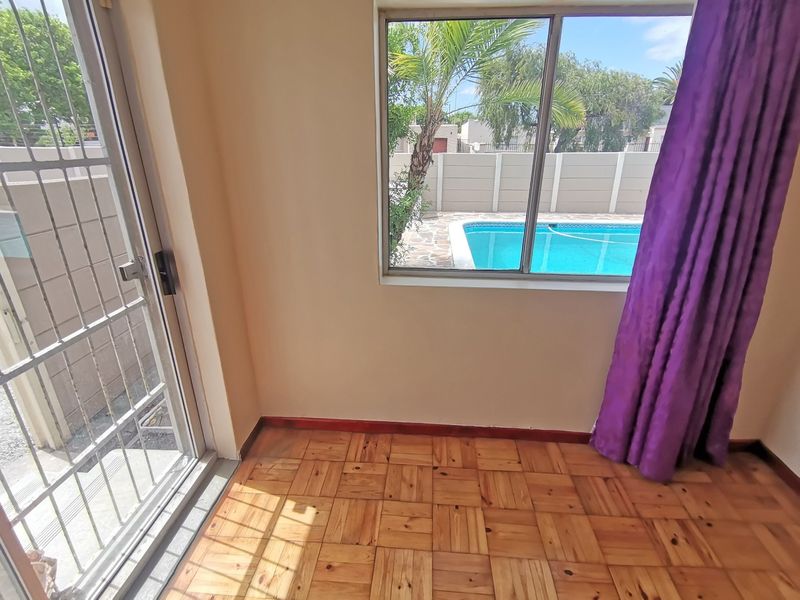 Empty living area featuring parquet flooring, a sliding door with security gate, and a window view overlooking the swimming pool.