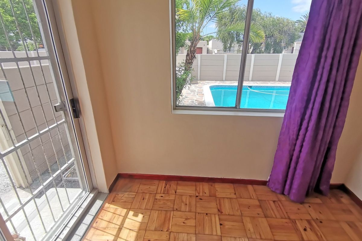 Empty living area featuring parquet flooring, a sliding door with security gate, and a window view overlooking the swimming pool.