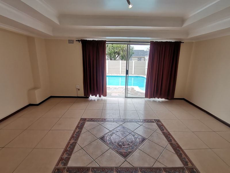 An empty living room featuring a tray ceiling, decorative tile flooring, and sliding glass doors providing direct access to the swimming pool area.