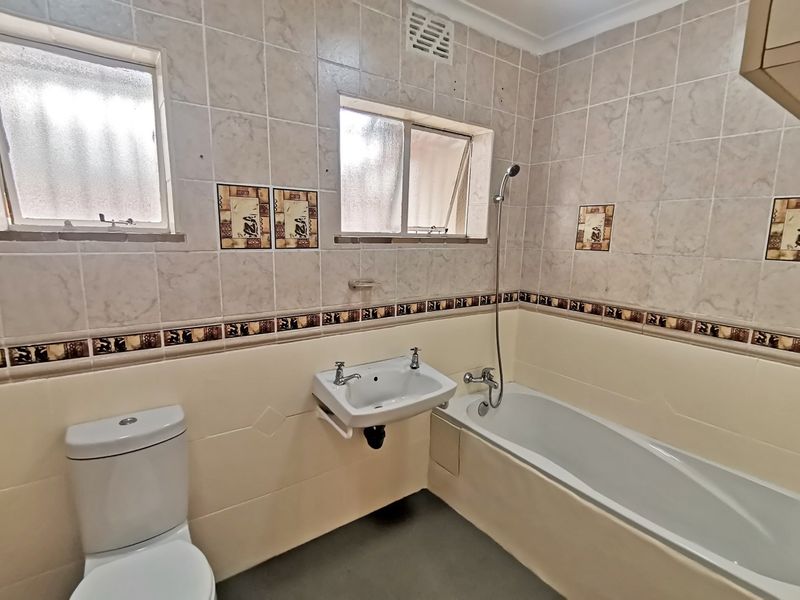 A functional bathroom featuring a bathtub with a handheld shower, a wall-mounted basin, and a toilet, finished with neutral wall tiling.