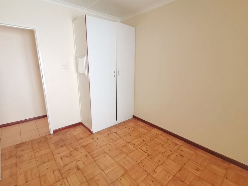 A clean, empty bedroom featuring classic parquet flooring and a built-in white wardrobe, offering a neutral canvas for personalization.