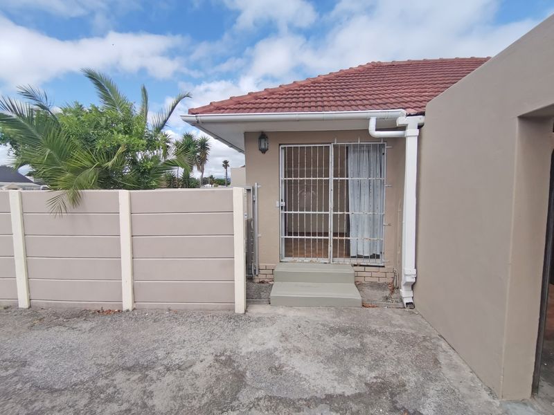 Rear exterior view showing a concrete boundary wall, security gate entrance, tiled roof, and concrete paving.