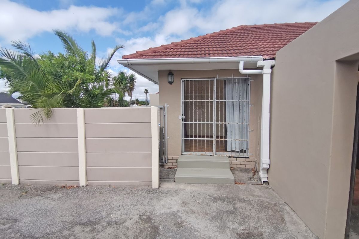 Rear exterior view showing a concrete boundary wall, security gate entrance, tiled roof, and concrete paving.