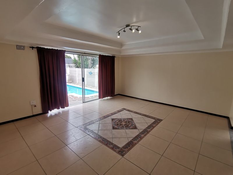 Spacious living room featuring a tray ceiling, ceramic tile flooring with a decorative inlay, and sliding glass doors providing access to the pool area.