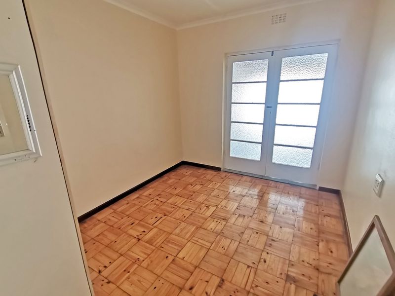 An empty bedroom featuring classic parquet flooring and double glass panel doors providing natural light and access to the exterior.