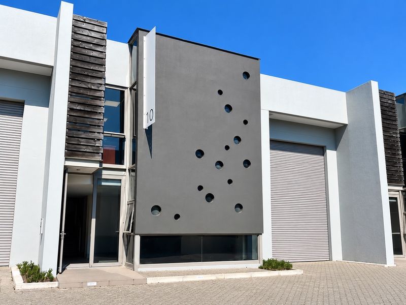Modern industrial unit featuring a striking grey facade with circular windows, large roller shutter doors, and professional glass entrance detailing.