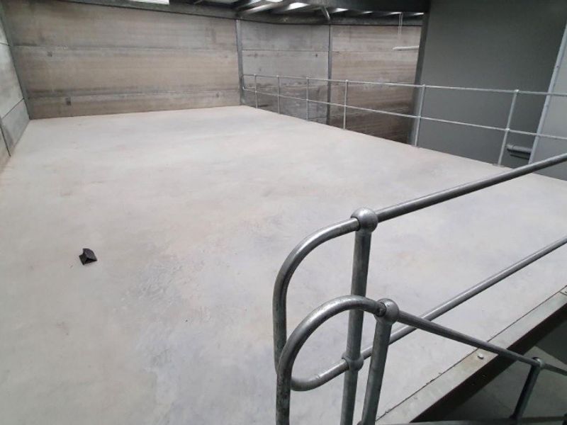 An industrial mezzanine level featuring concrete flooring, precast wall panels, and a secure metal safety railing, suitable for storage or additional workspace.