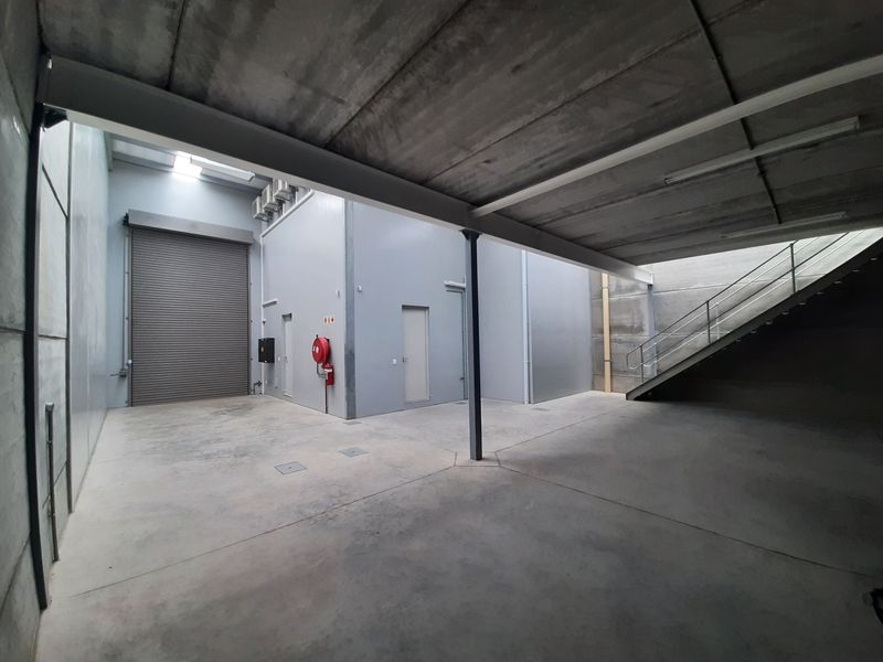 Spacious industrial garage area featuring a high roller shutter door, concrete flooring, and an integrated metal staircase leading to an upper level.