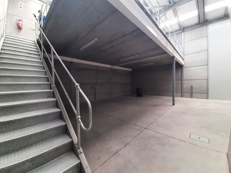 Spacious industrial utility area featuring a metal staircase leading to a mezzanine level, concrete flooring, and precast wall panels.