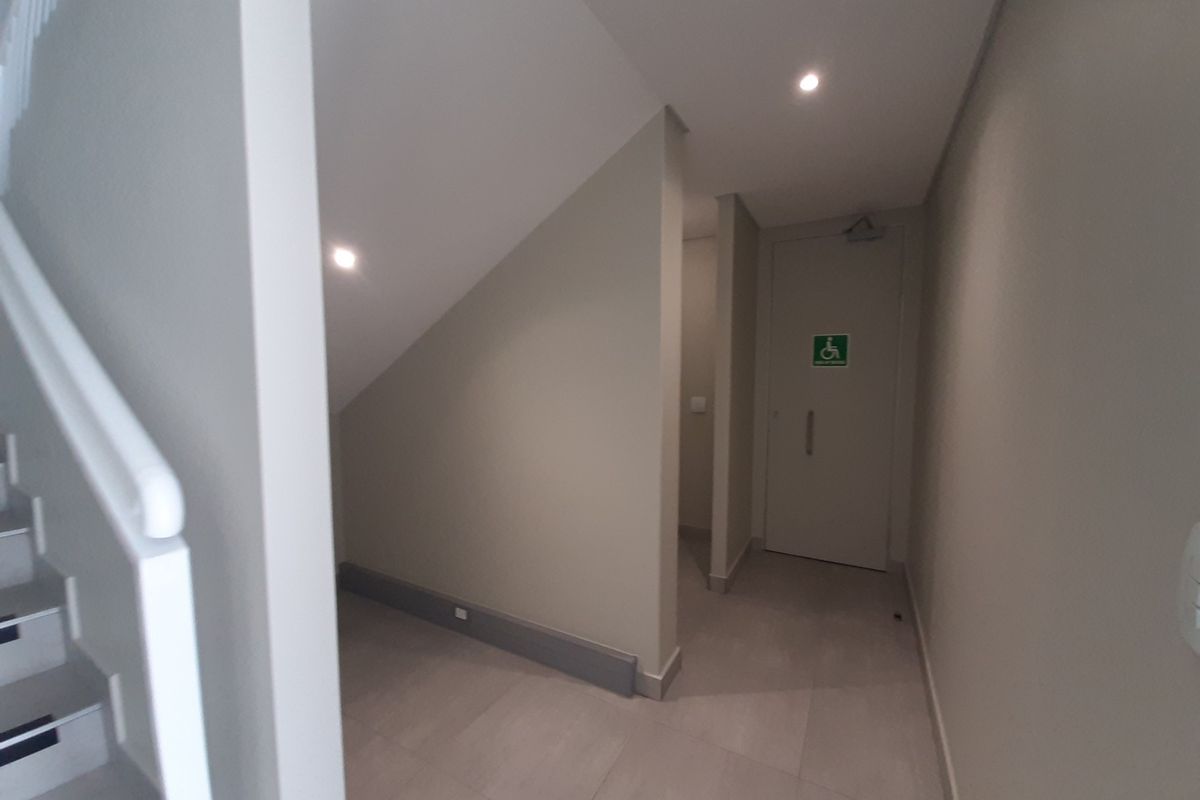 A clean, modern hallway featuring tiled flooring, recessed lighting, and an accessible doorway, with an adjacent staircase.
