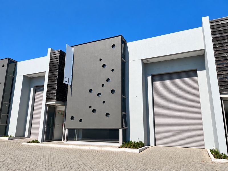 Modern industrial unit exterior featuring a contemporary facade with circular architectural detailing, roller shutter doors, and paved driveway access.