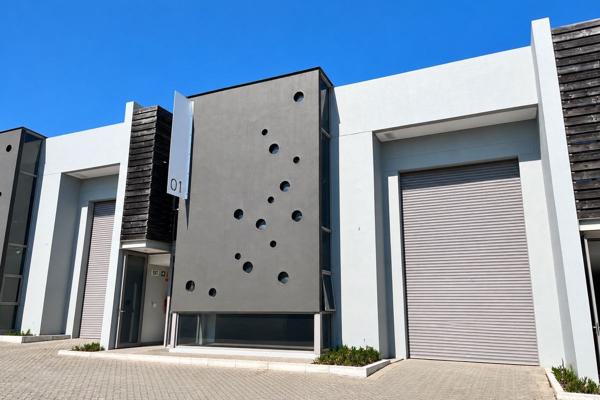 Modern industrial unit exterior featuring a contemporary facade with circular architectural detailing, roller shutter doors, and paved driveway access.