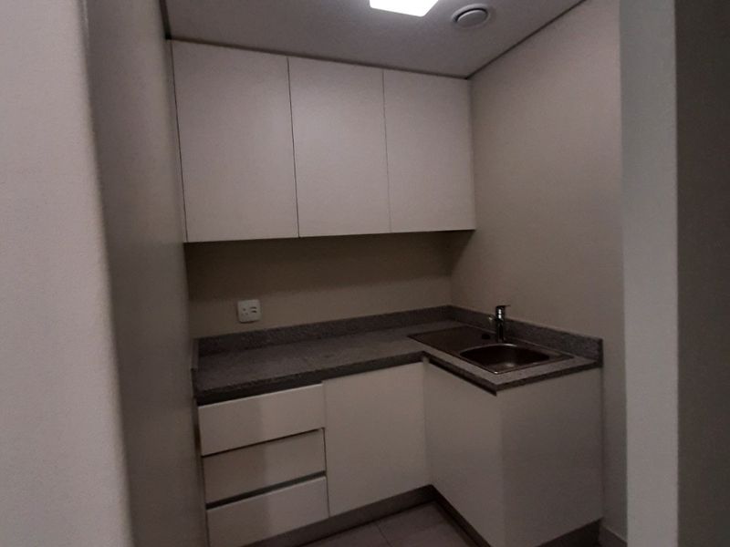 A compact, clean scullery or utility area featuring built-in white cabinetry, stone countertops, and a stainless steel sink.
