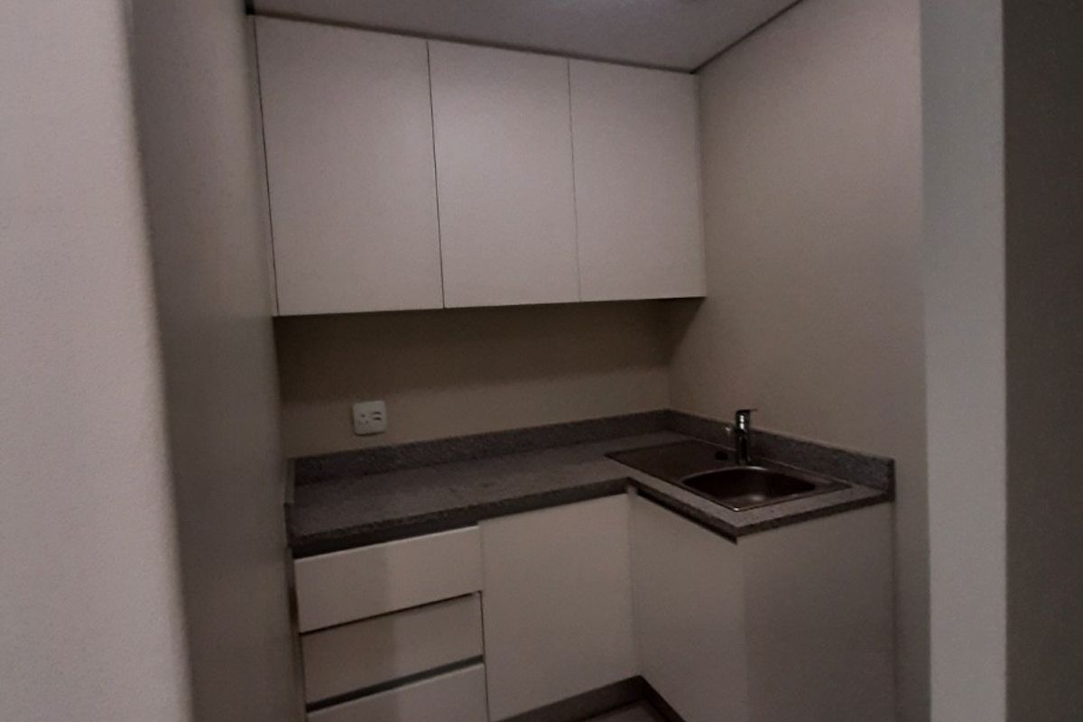 A compact, clean scullery or utility area featuring built-in white cabinetry, stone countertops, and a stainless steel sink.