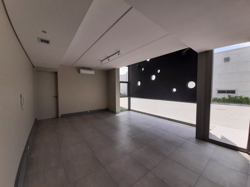 A modern, empty office space featuring large windows with unique circular cutouts, tiled flooring, and integrated air conditioning.