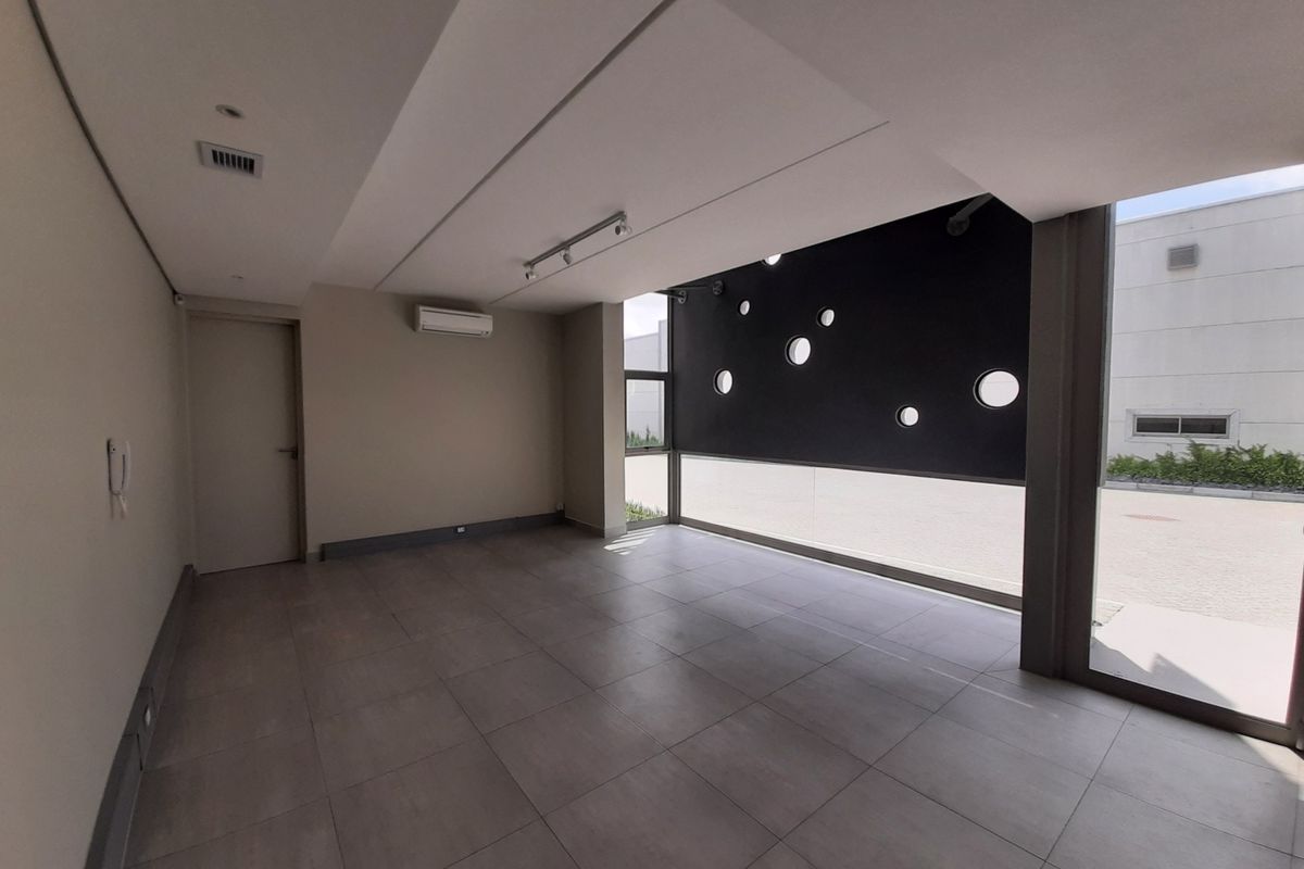 A modern, empty office space featuring large windows with unique circular cutouts, tiled flooring, and integrated air conditioning.