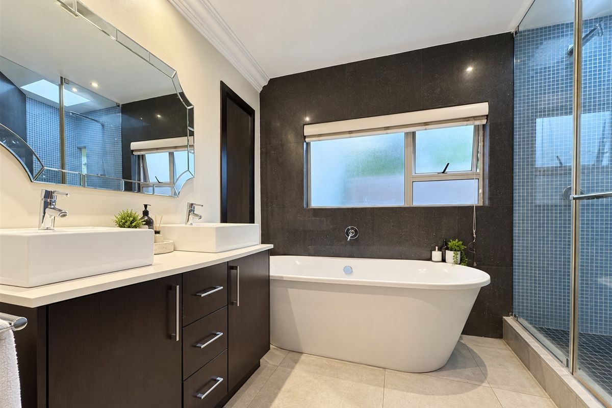 Modern bathroom featuring a double vanity, a sleek freestanding bathtub, and a separate glass-enclosed shower with stylish mosaic tile accents.
