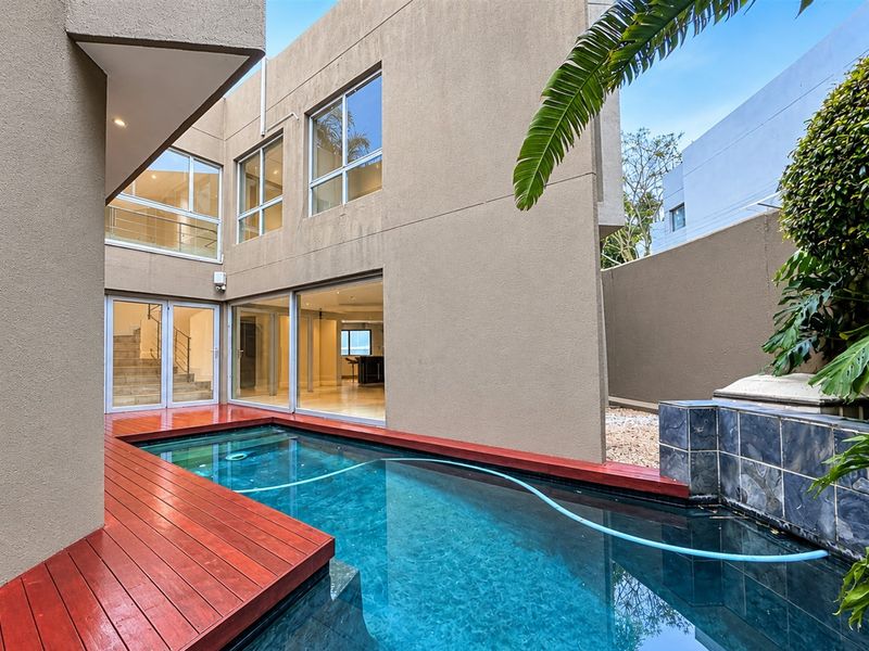 A modern rear courtyard featuring a swimming pool with timber decking, a tiled water feature, and direct access to the home via sliding glass doors.