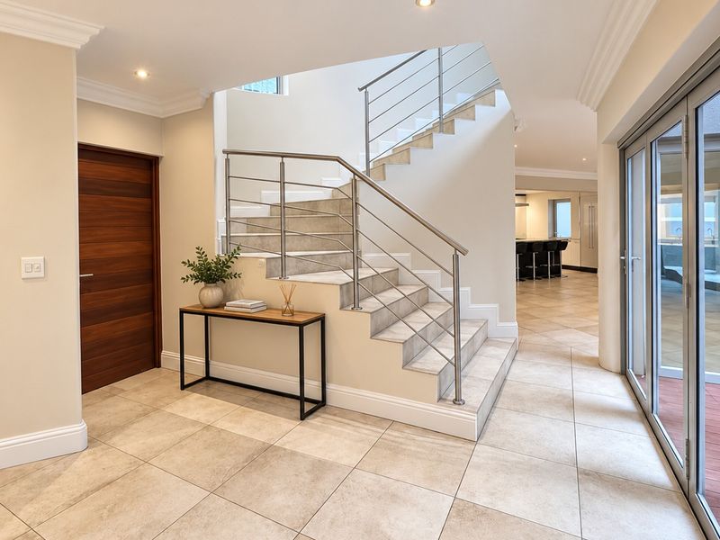 Spacious entrance hall featuring tiled flooring, a modern staircase with stainless steel railings, and large sliding glass doors leading to the exterior.