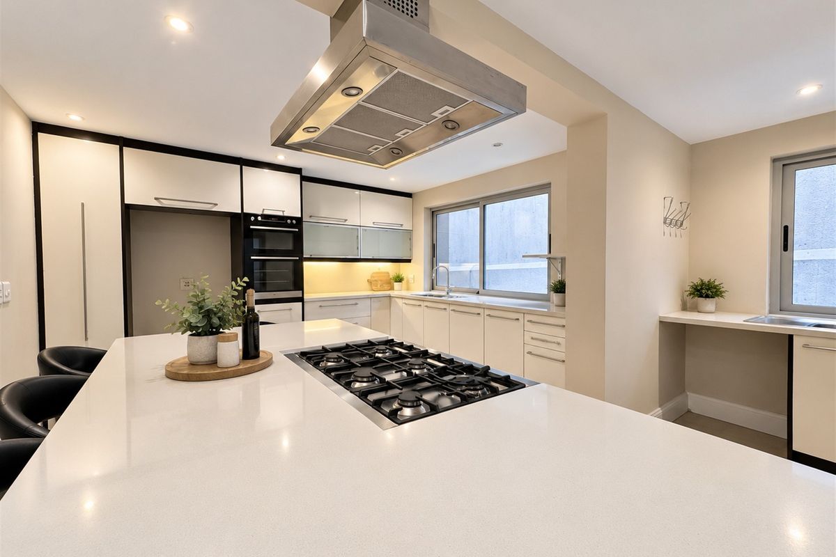 Modern kitchen featuring a large island with a gas cooktop, stainless steel extractor fan, built-in oven, and sleek cabinetry with quartz countertops.