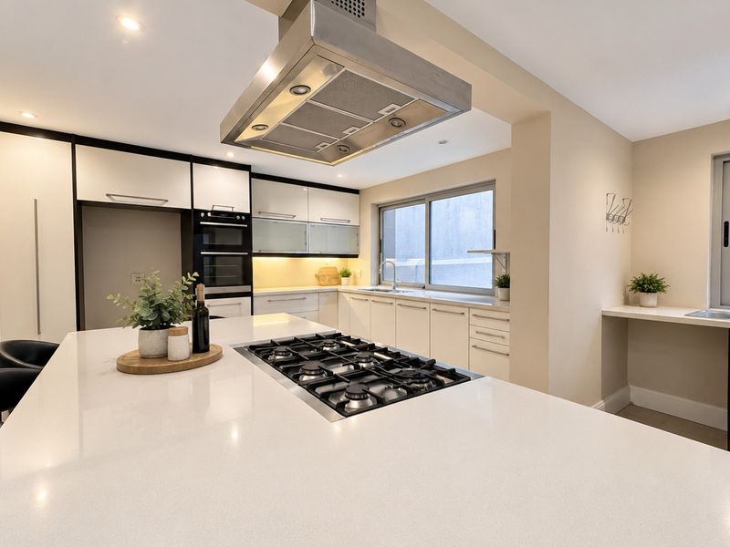 Modern kitchen featuring a large island with a gas cooktop, stainless steel extractor fan, built-in oven, and sleek cabinetry with quartz countertops.
