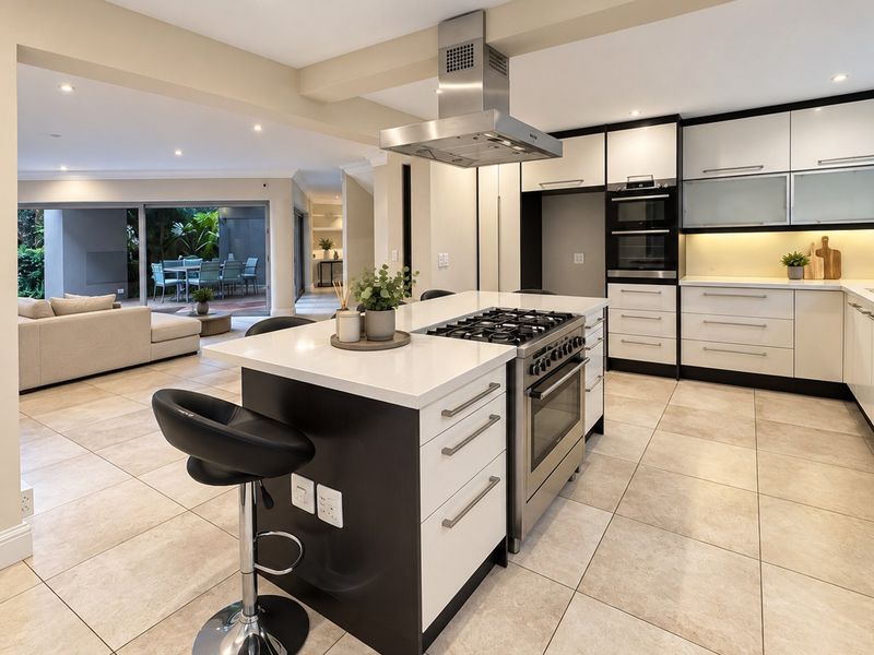 Modern open-plan kitchen featuring a central island with gas cooktop, sleek cabinetry, stone countertops, and seamless flow to the outdoor patio area.