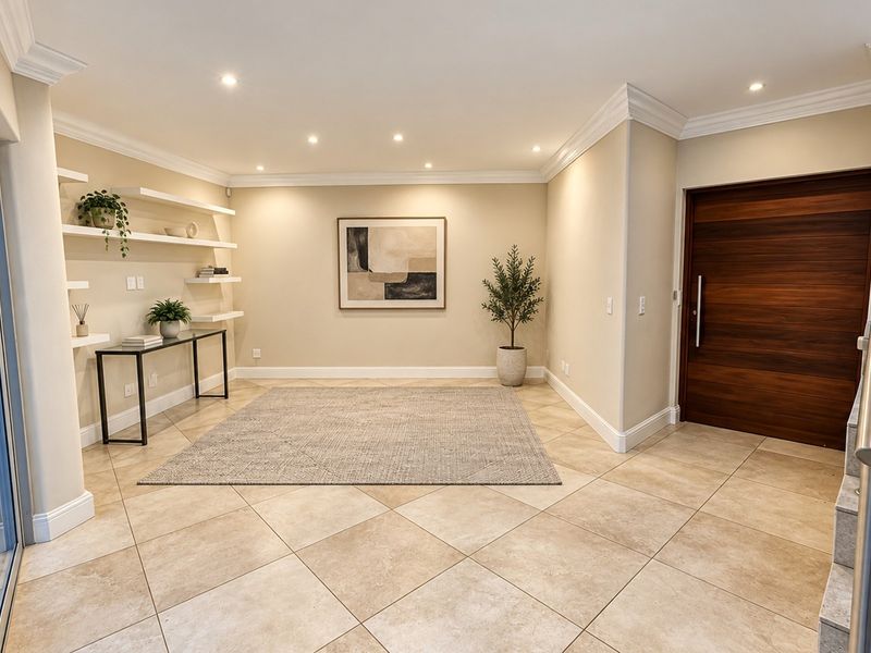 Spacious entrance hall featuring neutral tiled flooring, recessed downlighting, elegant crown molding, and a solid wood front door with built-in display shelving.