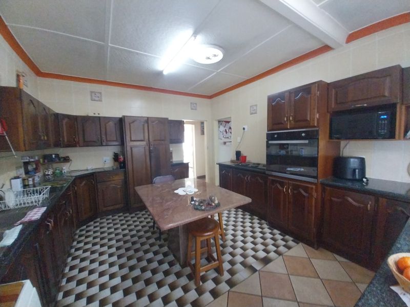 A spacious kitchen featuring traditional dark wood cabinetry, stone countertops, built-in oven and microwave, and a central island with tiled flooring throughout.