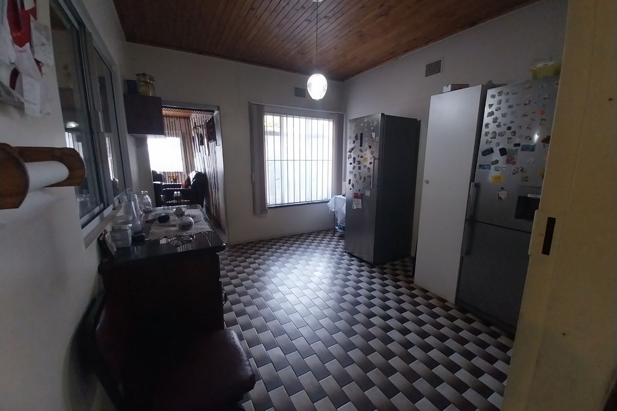 A functional kitchen area featuring a timber-paneled ceiling, tiled flooring, and security bars on the windows, offering a dated but practical layout.