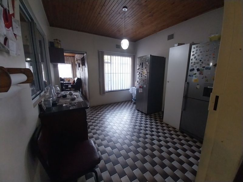 A functional kitchen area featuring a timber-paneled ceiling, tiled flooring, and security bars on the windows, offering a dated but practical layout.