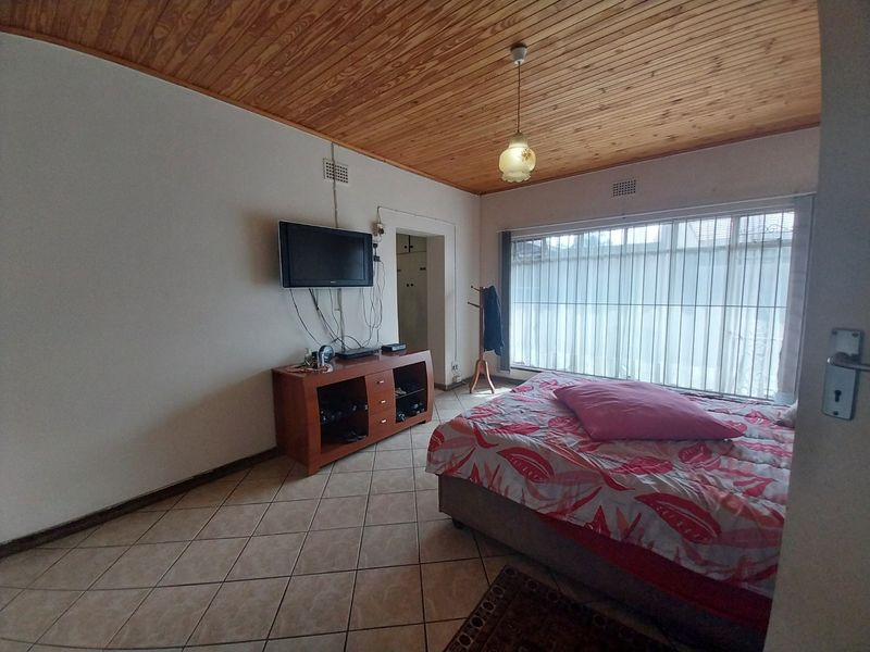 Bedroom featuring ceramic floor tiles and a timber tongue and groove ceiling, with security bars on the window and an integrated cupboard.