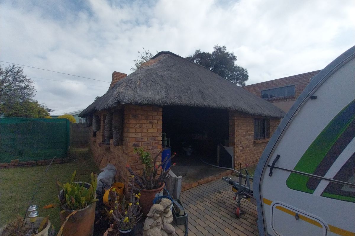 A detached face brick outbuilding featuring a traditional thatch roof, situated in a rear garden setting with paved access.