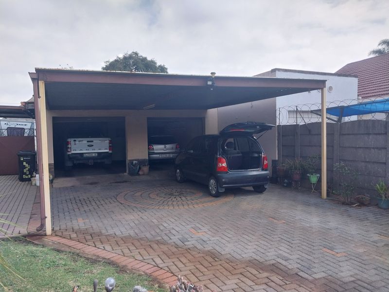 A double carport with a paved driveway and perimeter walling featuring security razor wire.