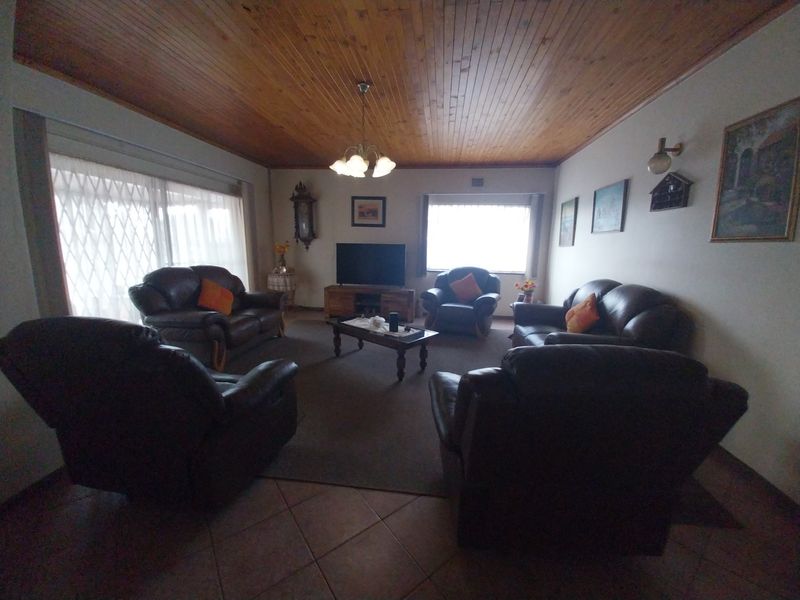 Spacious living room featuring a warm timber tongue and groove ceiling, ceramic tiled flooring, and natural light through large windows with security gates.