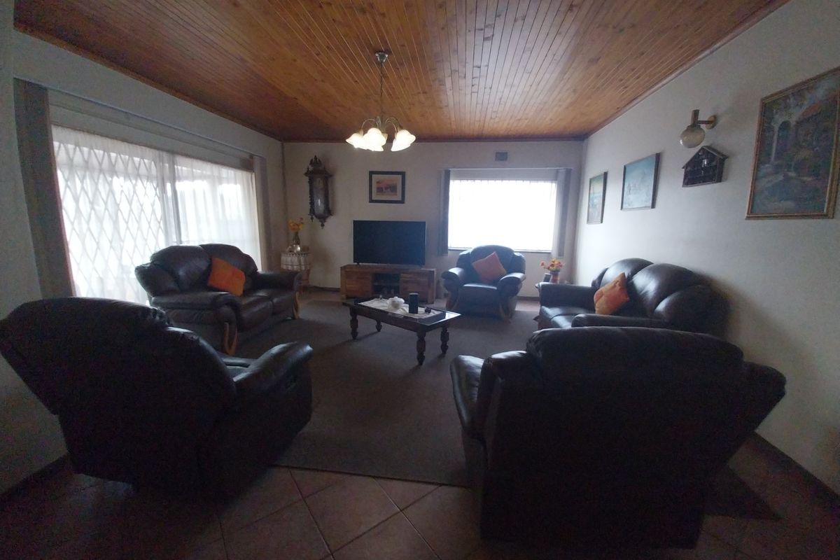 Spacious living room featuring a warm timber tongue and groove ceiling, ceramic tiled flooring, and natural light through large windows with security gates.