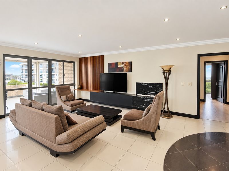 Spacious living room featuring a modern built-in media console, marble fireplace detail, timber slat wall feature, and large sliding doors leading to the balcony.