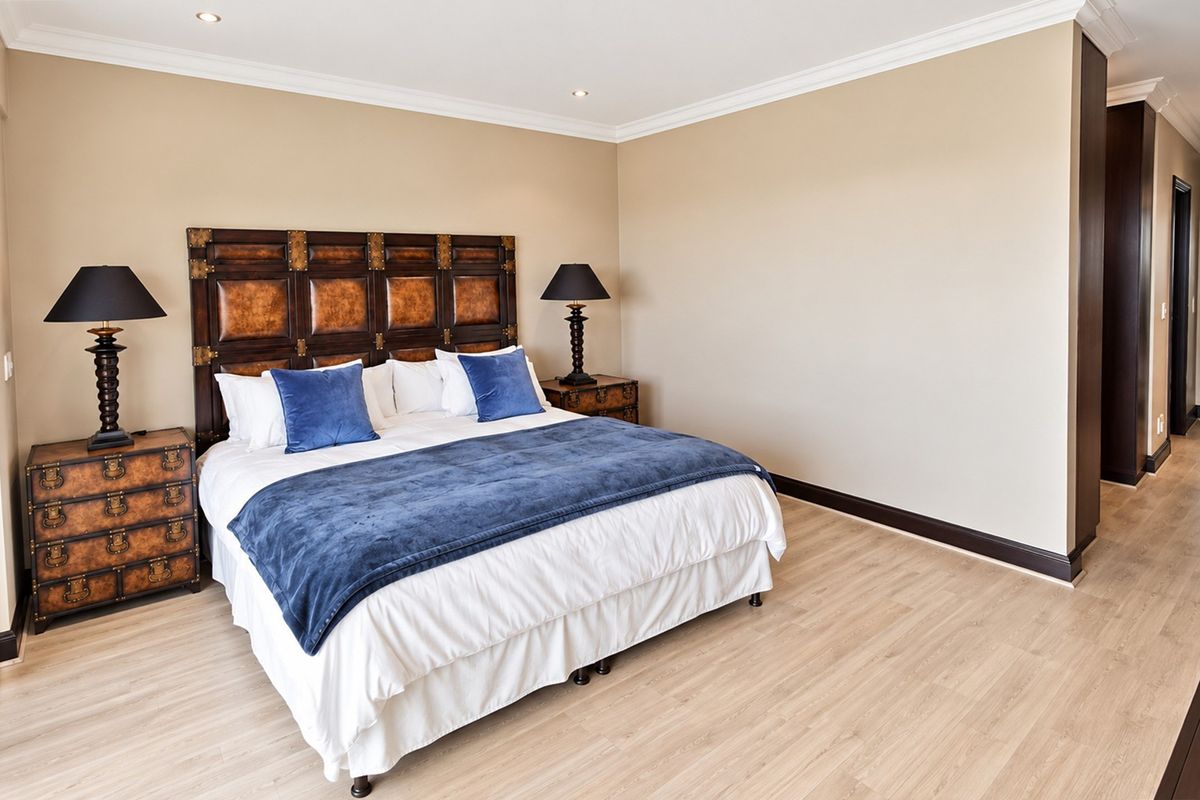 A spacious bedroom featuring light-toned laminate flooring, crown molding, and recessed downlighting, creating a clean and well-maintained living environment.