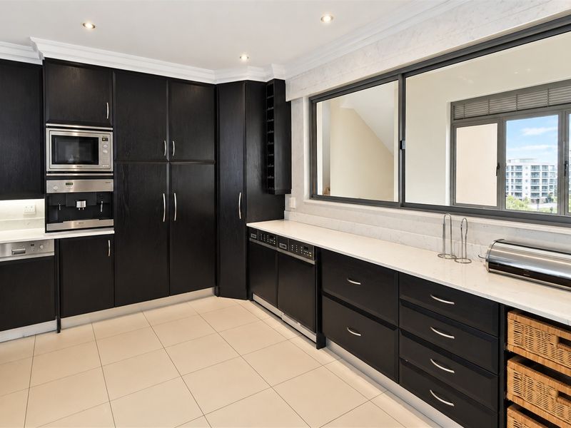 Modern kitchen featuring dark wood cabinetry, stone countertops, integrated appliances, and large windows providing natural light and exterior views.