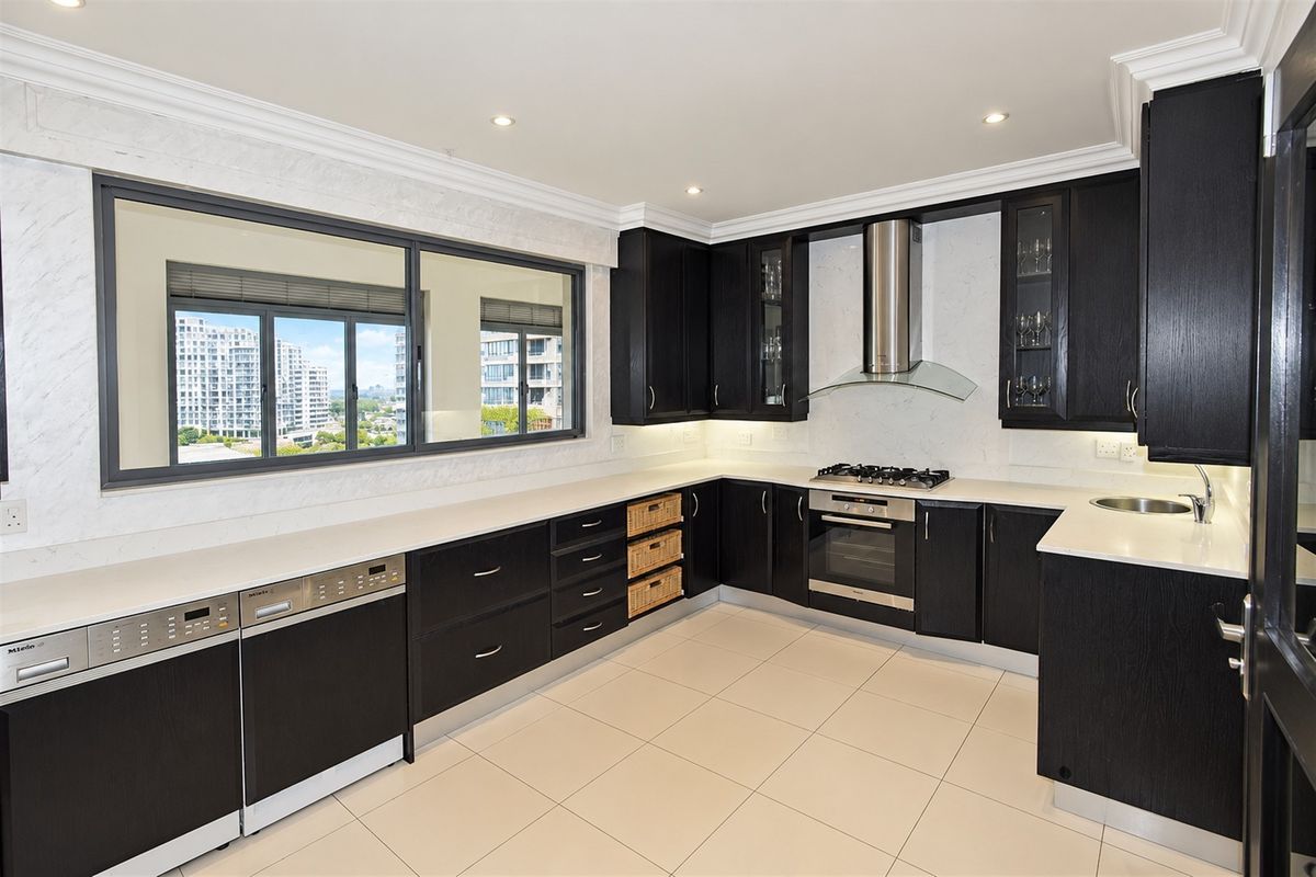 Modern kitchen featuring dark wood cabinetry, stone countertops, integrated appliances, gas hob, and large windows with city views.