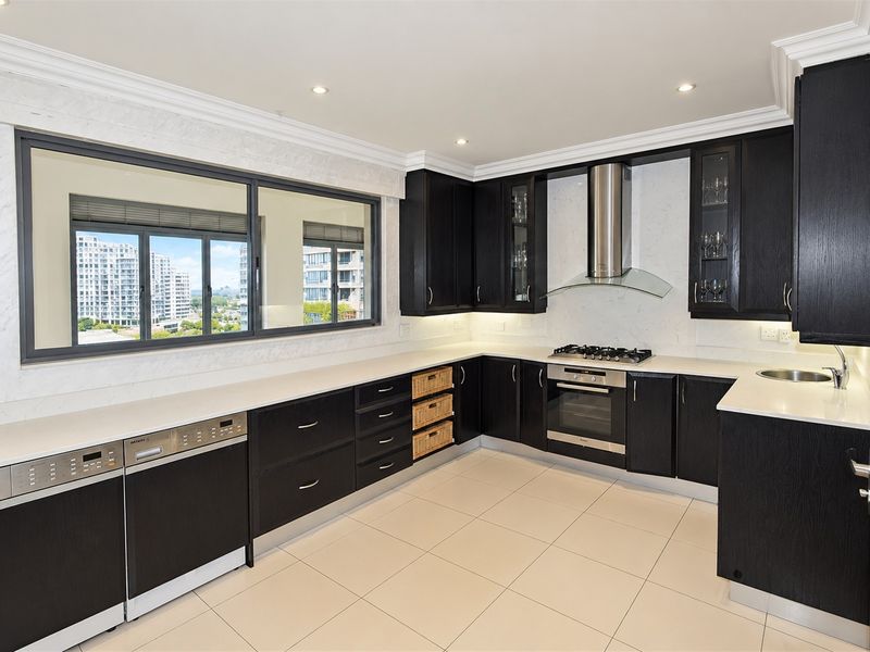 Modern kitchen featuring dark wood cabinetry, stone countertops, integrated appliances, gas hob, and large windows with city views.