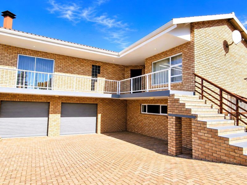 A well-maintained double-story brick house featuring a paved driveway, double garage, and an elevated balcony accessible via an external staircase.