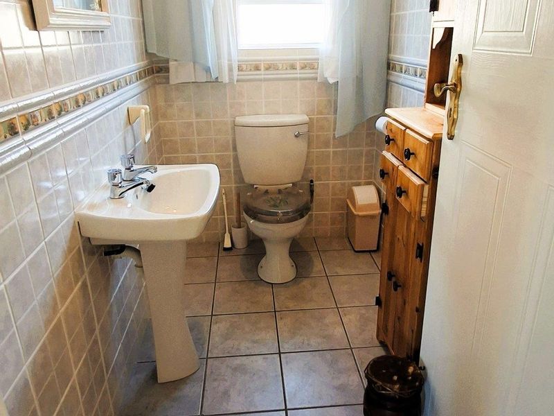 A functional bathroom featuring tiled walls and flooring, a pedestal basin, and a standard toilet, offering a clean and practical layout.