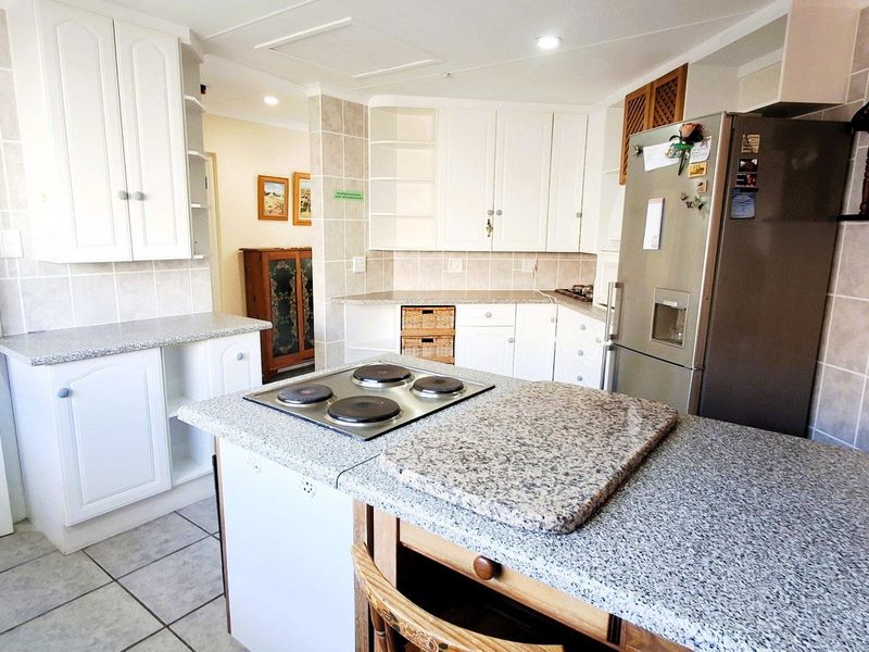 Functional kitchen featuring granite countertops, ample built-in cabinetry, a central island with an electric hob, and neutral tiled finishes throughout.