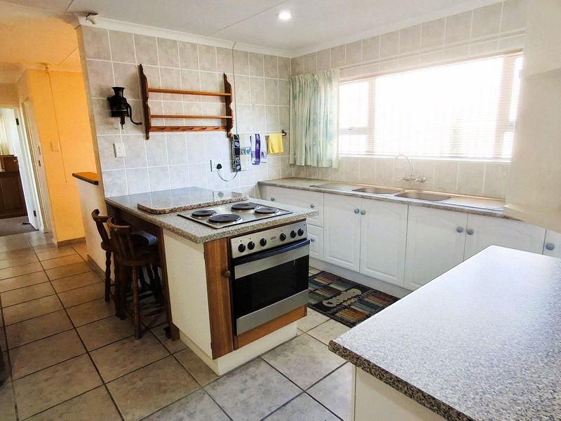 A functional kitchen featuring built-in cabinetry, a double sink, tiled backsplash, and a central island with an integrated electric oven and hob.