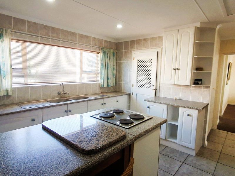 A functional kitchen featuring built-in cabinetry, laminate countertops, a double sink, and a central island with an integrated electric hob.