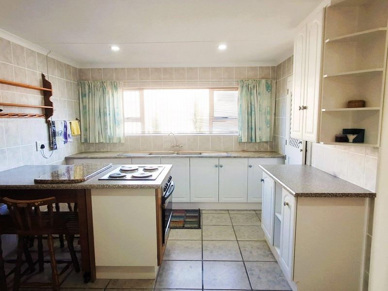 A functional kitchen featuring white cabinetry, laminate countertops, tiled backsplash, and integrated cooking appliances with ample storage and natural light.