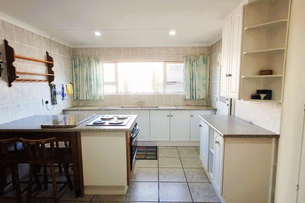 A functional kitchen featuring white cabinetry, laminate countertops, tiled backsplash, and integrated cooking appliances with ample storage and natural light.