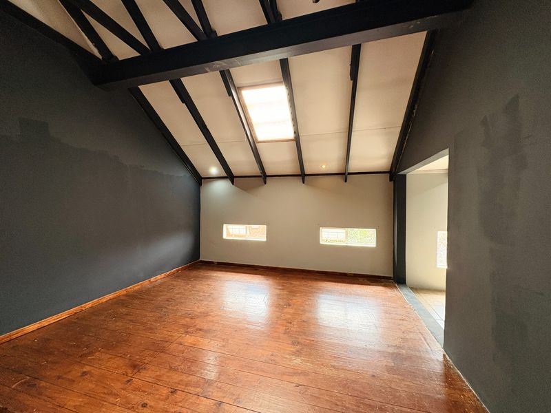 Spacious bedroom featuring exposed timber beams, a skylight, and warm timber flooring, offering a unique architectural character ready for personalization.