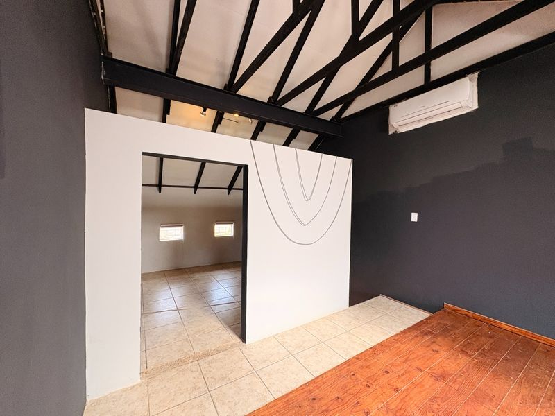 An empty bedroom featuring exposed roof trusses, a split-system air conditioner, and a mix of tiled and timber flooring with a central partition wall.