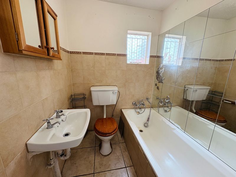 A dated bathroom featuring a pedestal basin, toilet, and bathtub with tiled walls and floor, offering potential for a modern renovation.